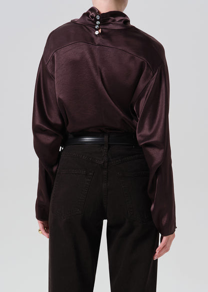A person shown from the back wearing a dark plum satin long-sleeve top with decorative buttons at the collar and black pants, against a grey background.