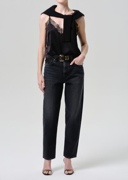 Person wearing a black sleeveless top with lace detail and high-waisted black jeans on a grey background
