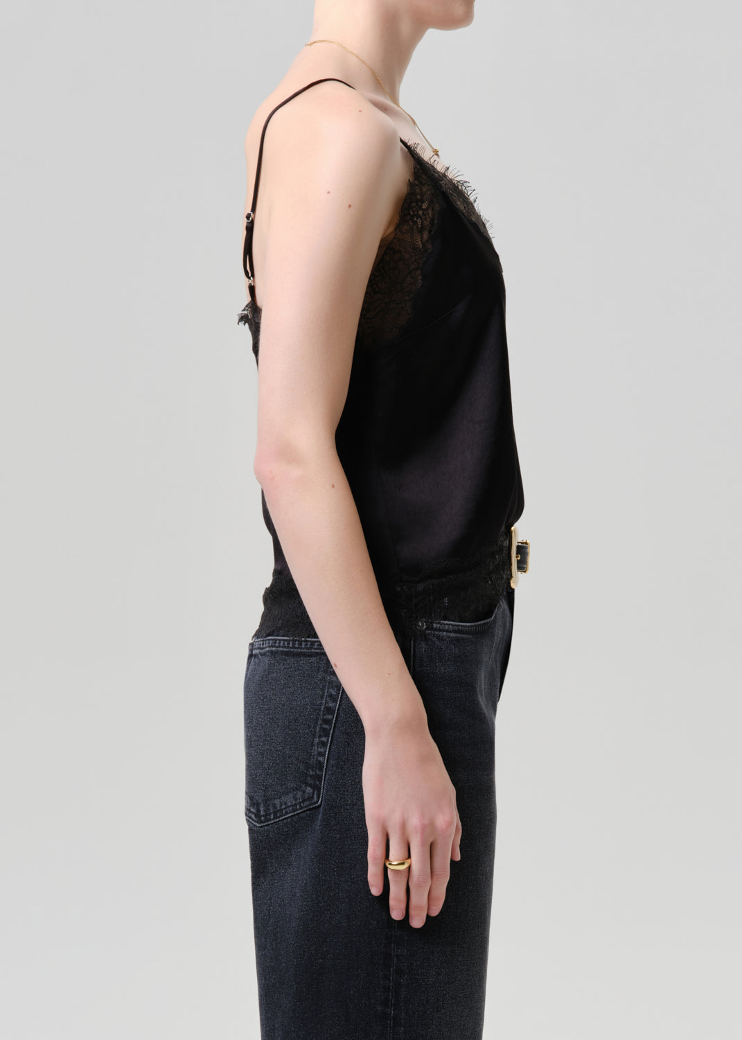 Person wearing a black sleeveless top and dark jeans on a grey background