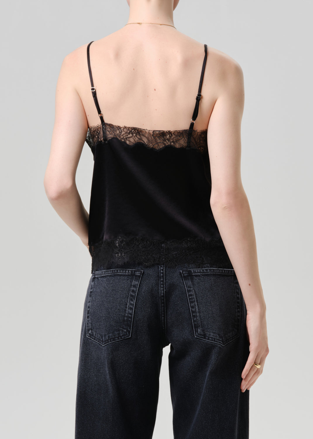 Person wearing a black lace-trimmed top and dark jeans on a grey background