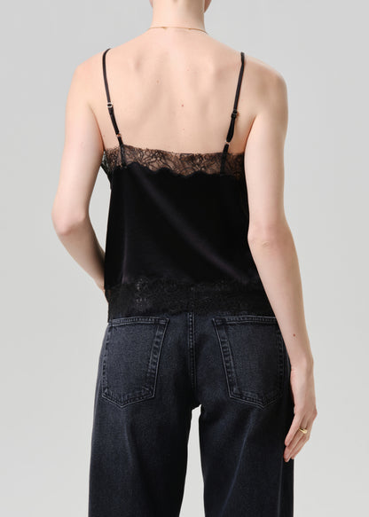 Person wearing a black lace-trimmed top and dark jeans on a grey background