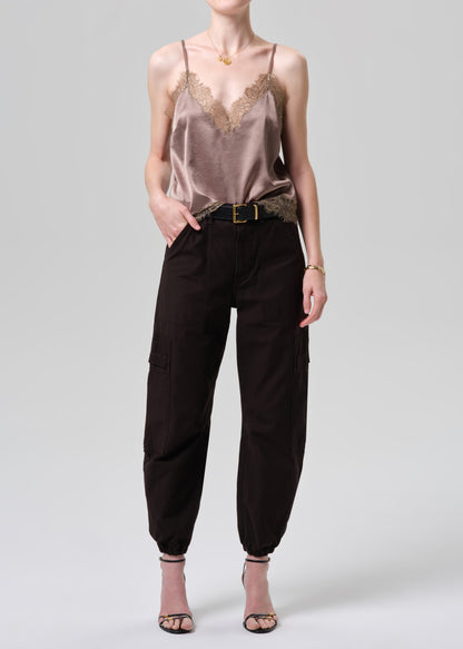 Woman wearing a beige lace camisole and black cargo pants on a grey background