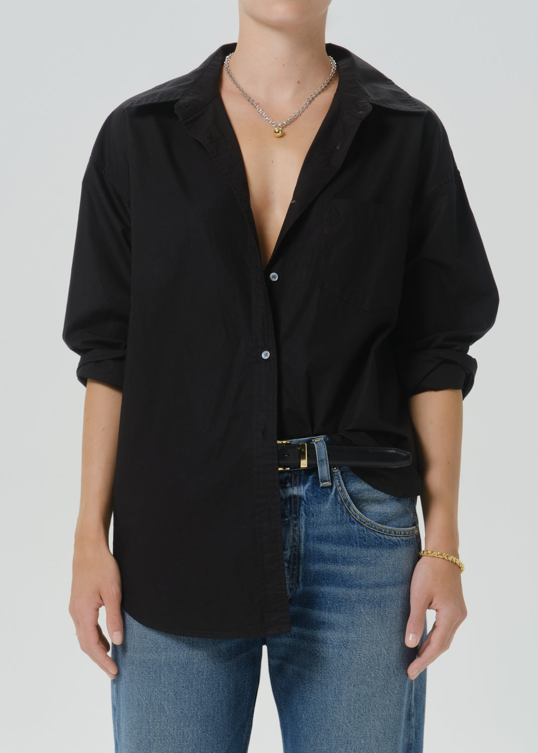 A person wearing an oversized black button-front shirt with rolled sleeves and blue jeans, shown from neck to upper thighs against a grey background.
