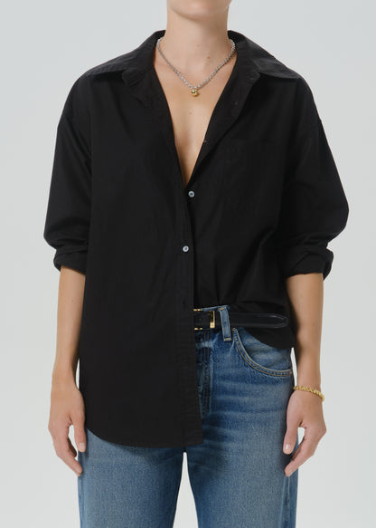 A person wearing an oversized black button-front shirt with rolled sleeves and blue jeans, shown from neck to upper thighs against a grey background.