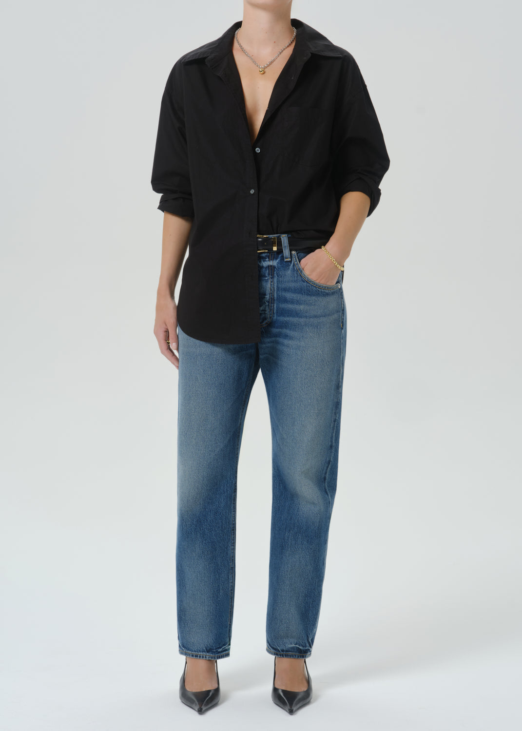A model wearing a black button-up shirt and blue jeans, standing against a grey background.