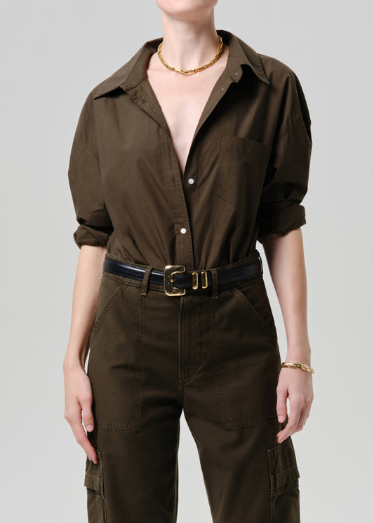 Person wearing a brown jumpsuit with a belt on a grey background