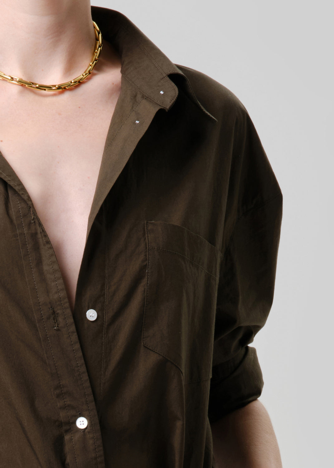 Brown button-up shirt with a gold necklace on a grey background