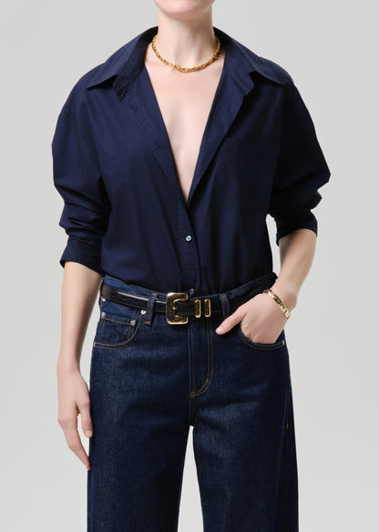 Person wearing a navy blue shirt and dark jeans on a grey background