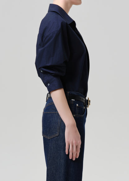 Person wearing a navy shirt and dark jeans on a grey background