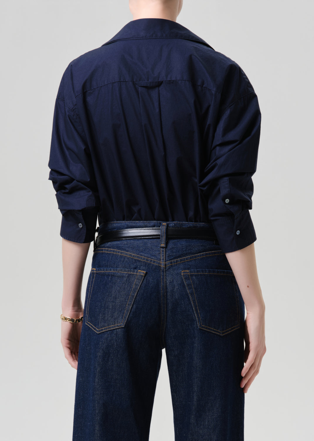 Person wearing a navy blue shirt and dark jeans on a grey background