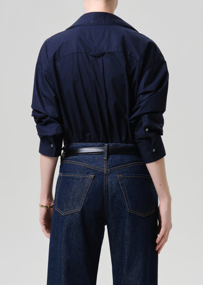 Person wearing a navy blue shirt and dark jeans on a grey background