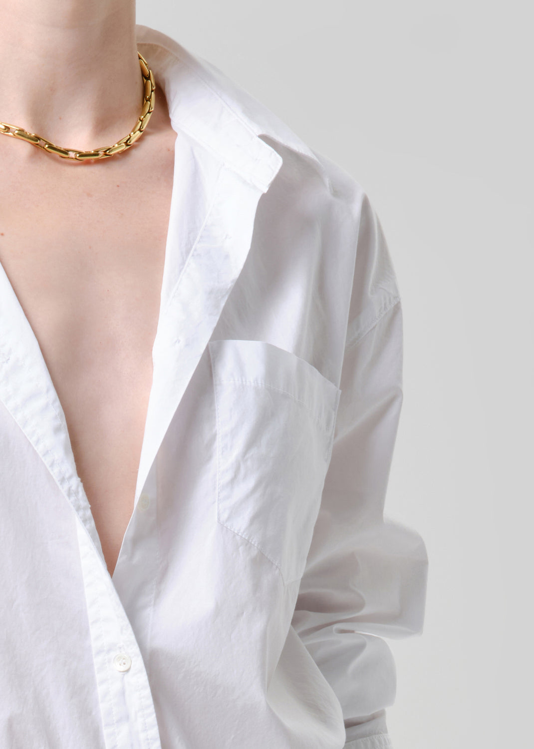 White shirt with a gold chain necklace on a grey background