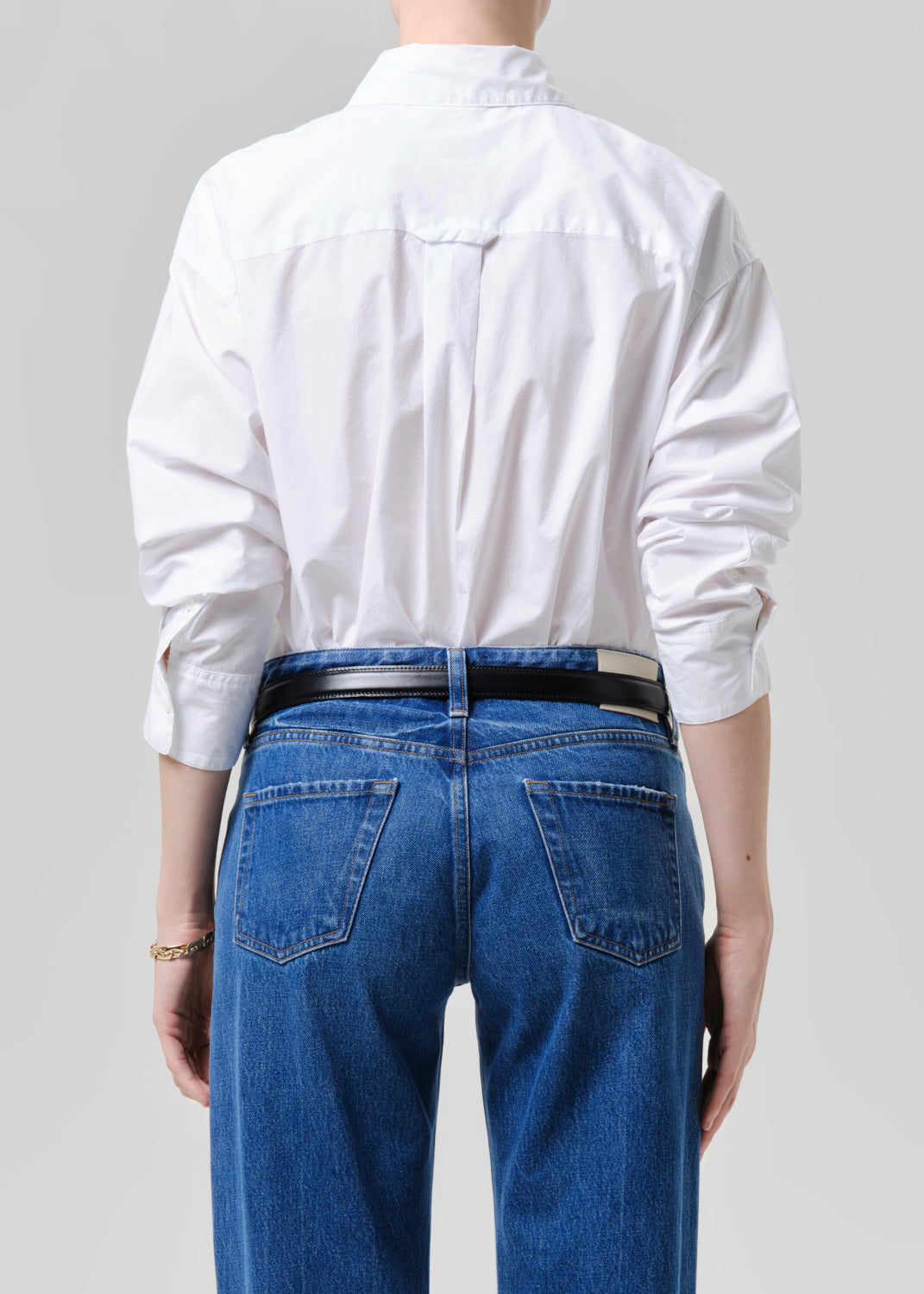 Person wearing a white shirt and blue jeans from behind on a grey background
