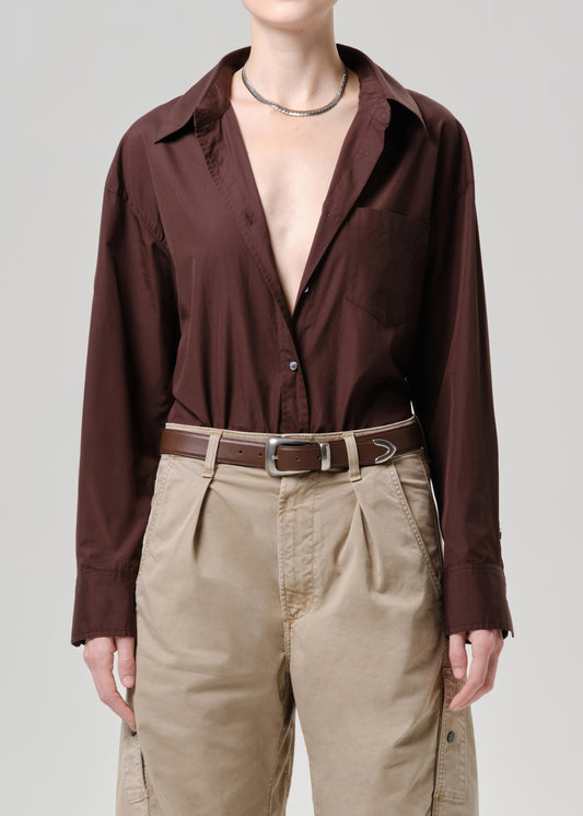Person wearing a brown button-up shirt and beige pants on a grey background