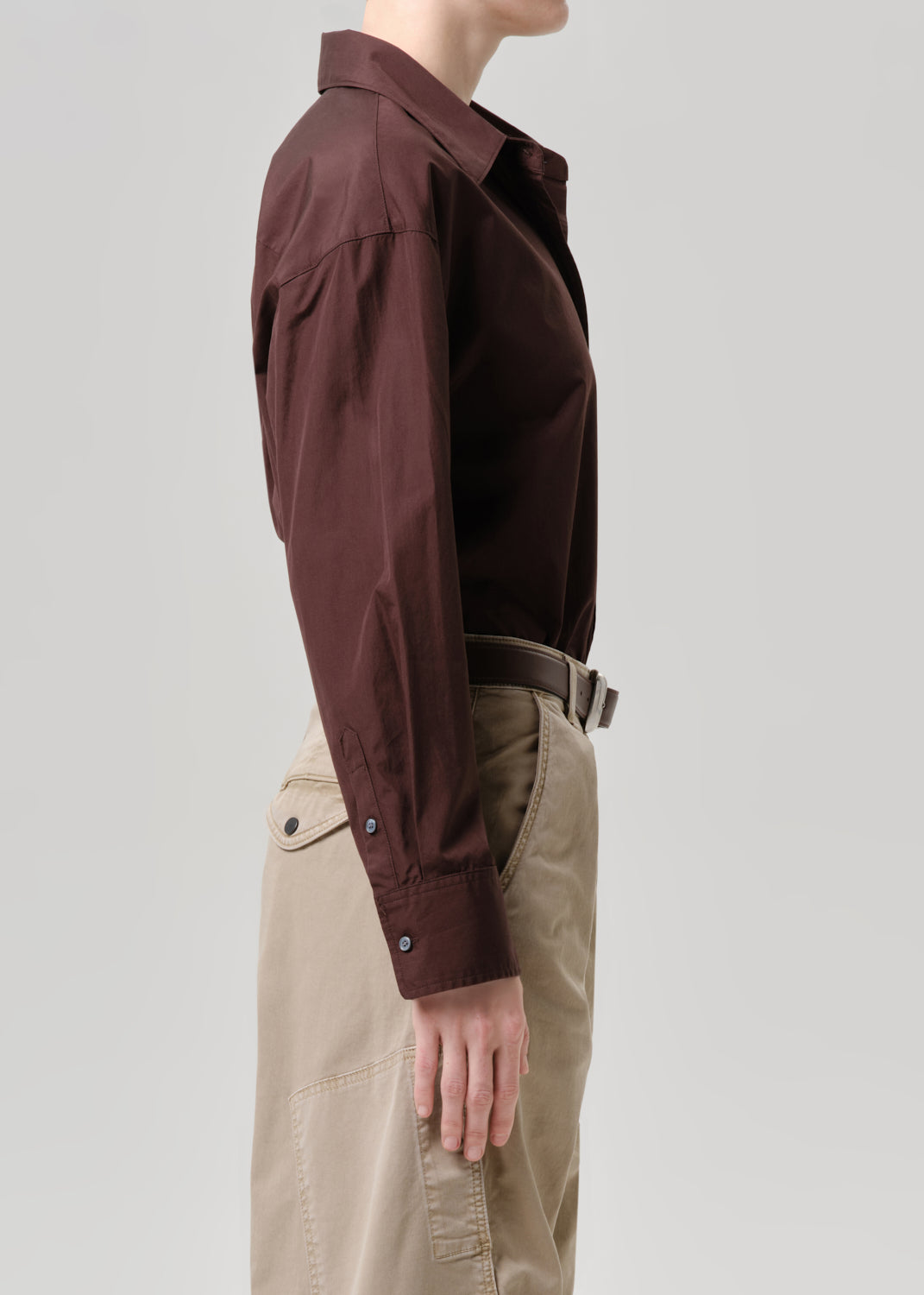 Person wearing a brown shirt and beige pants on a grey background