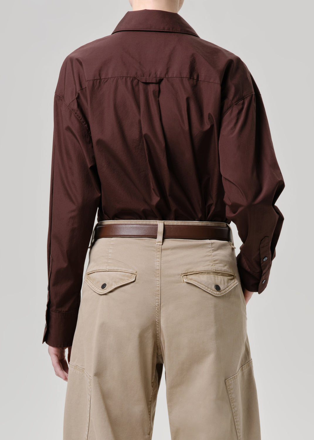 Person wearing a brown shirt and beige pants on a grey background