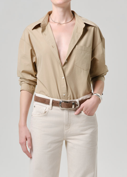 Person wearing a beige button-up shirt and light-colored pants on a grey background