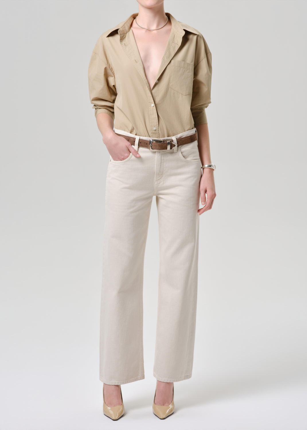 Person wearing a beige shirt and white pants on a grey background