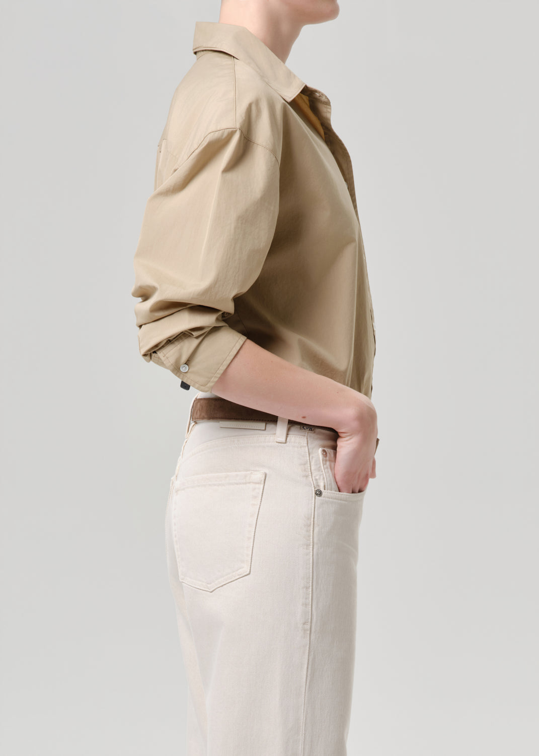 Person wearing a beige shirt and light-colored pants on a grey background