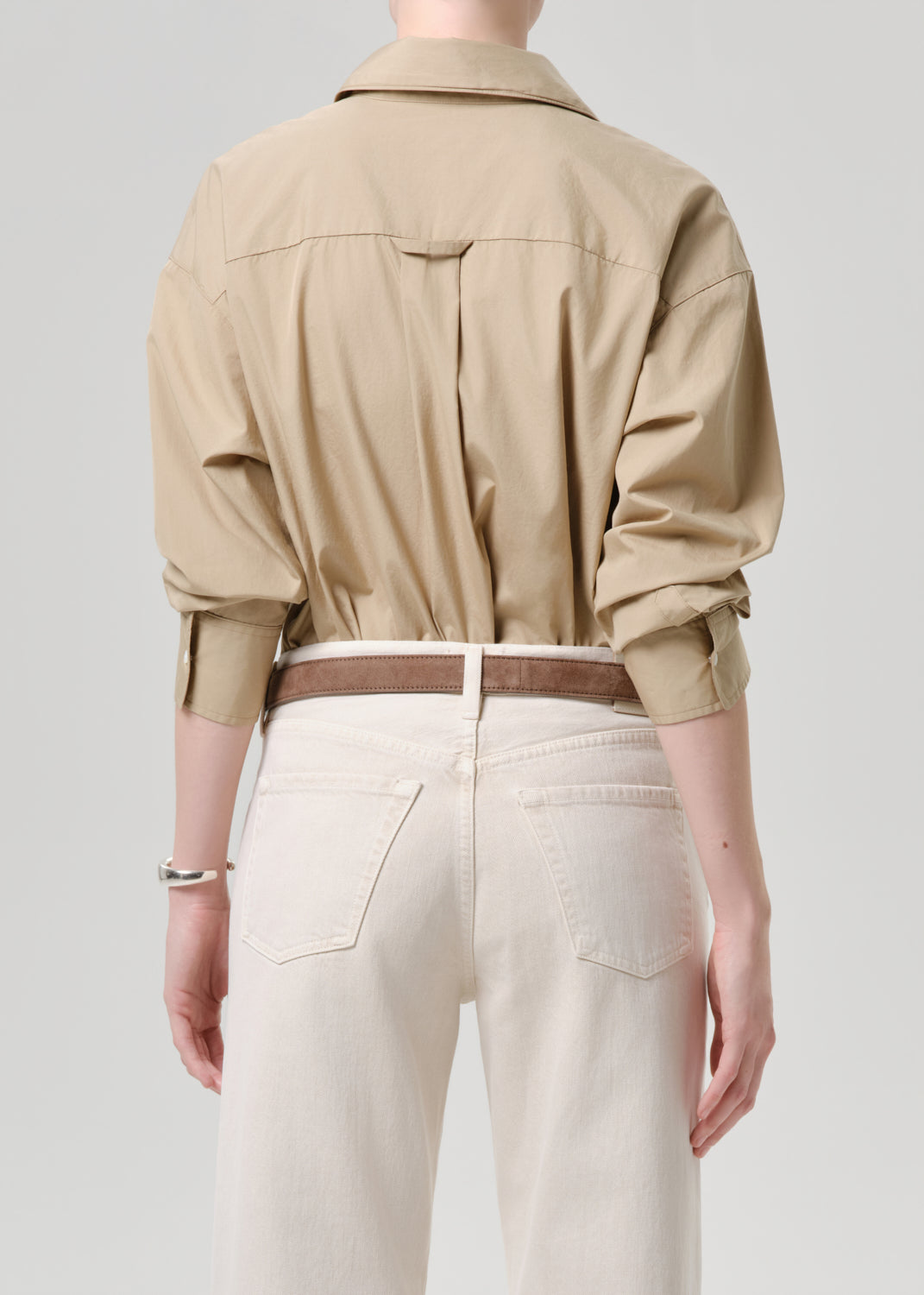 Person wearing a beige shirt and white pants on a grey background