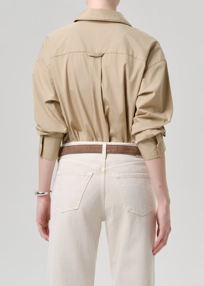 Person wearing a beige shirt and white pants on a grey background
