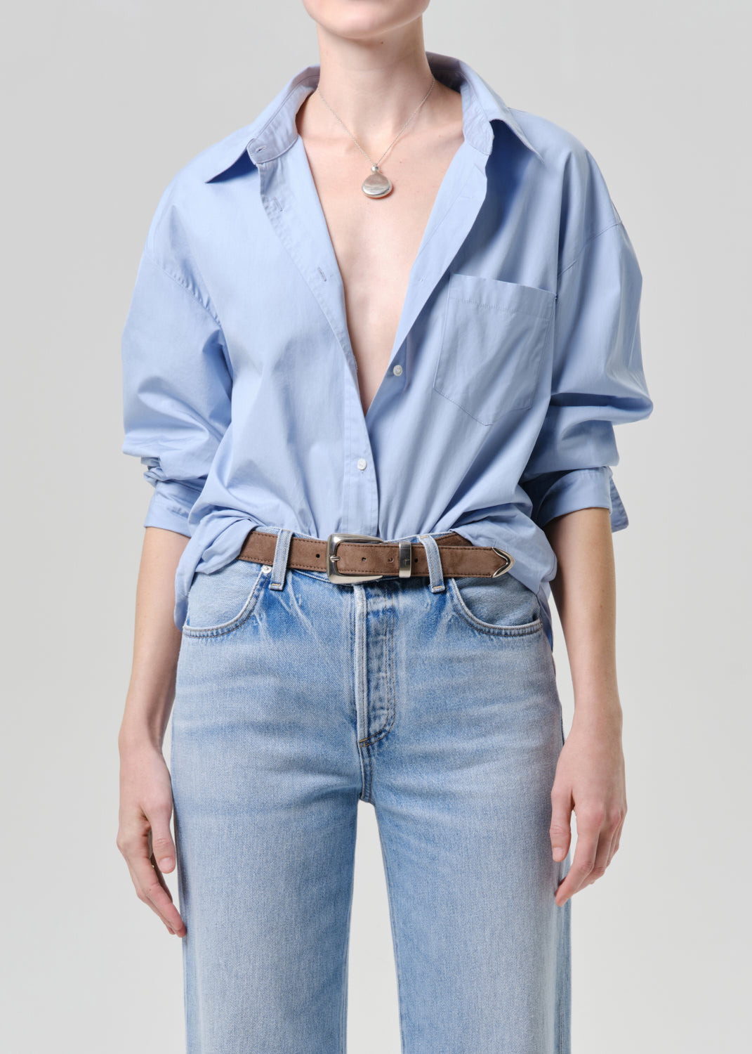 Person wearing a light blue shirt with rolled-up sleeves and light blue jeans on a grey background