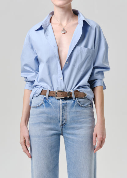 Person wearing a light blue shirt with rolled-up sleeves and light blue jeans on a grey background