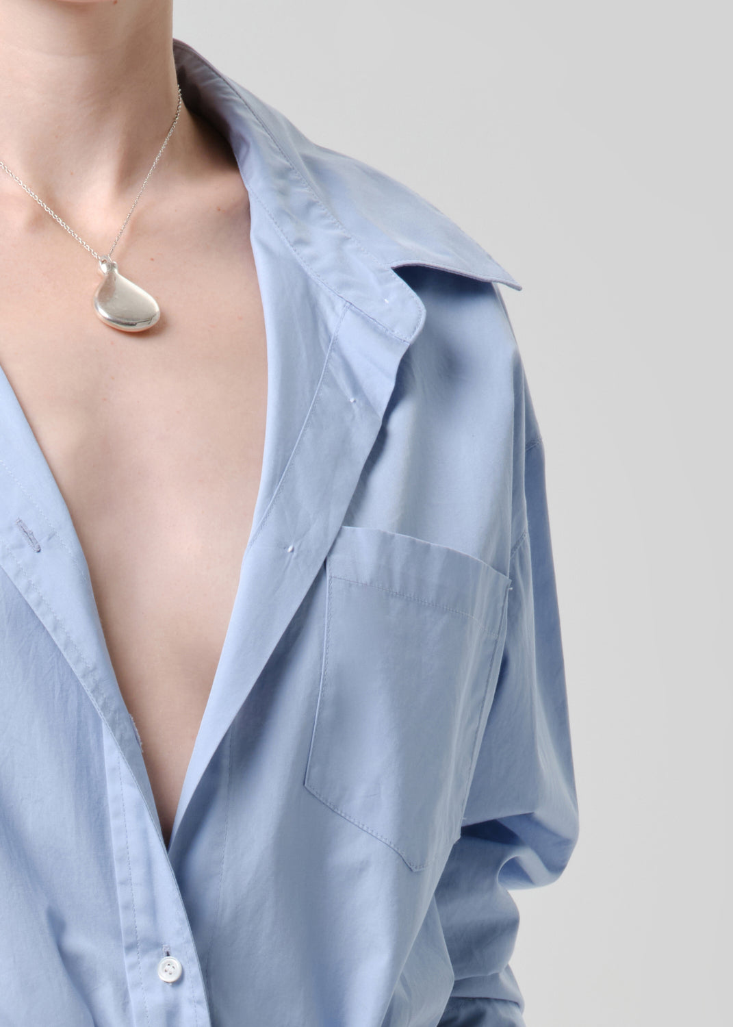 Light blue shirt with a necklace on a grey background