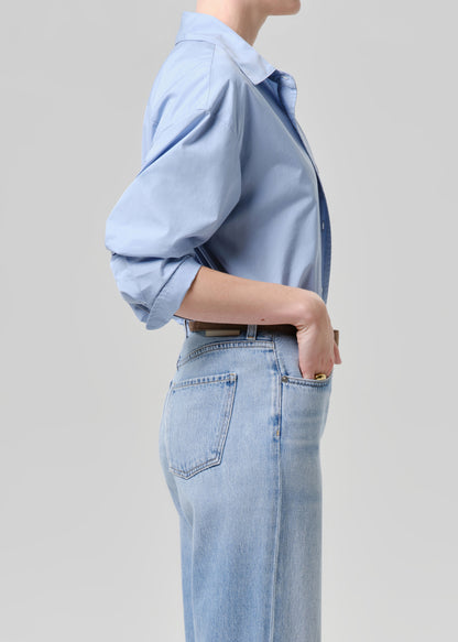 Person wearing a light blue shirt and jeans on a grey background