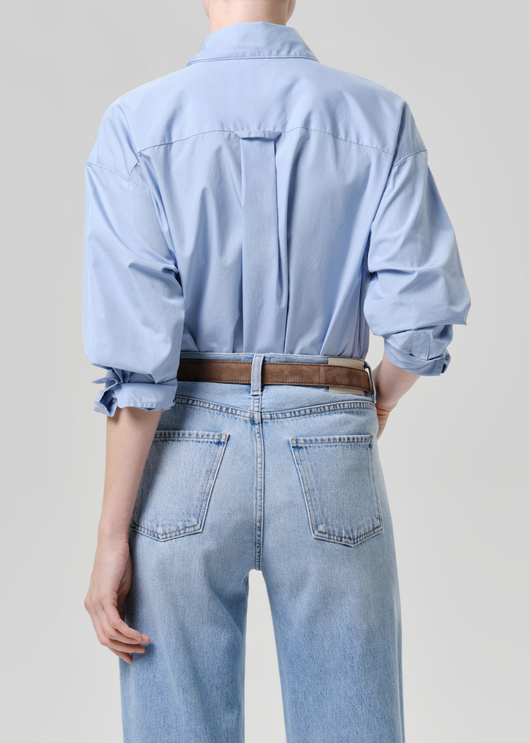Person wearing a light blue denim shirt and jeans on a grey background
