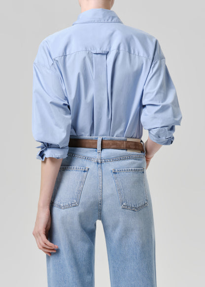 Person wearing a light blue denim shirt and jeans on a grey background