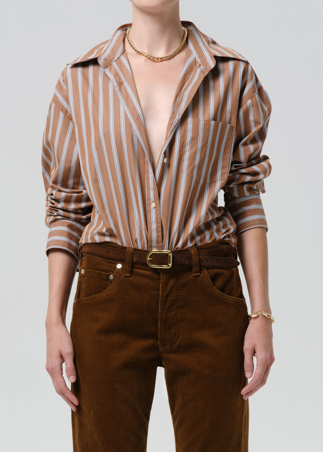 Person wearing a brown and white striped shirt with rolled-up sleeves and brown pants on a grey background