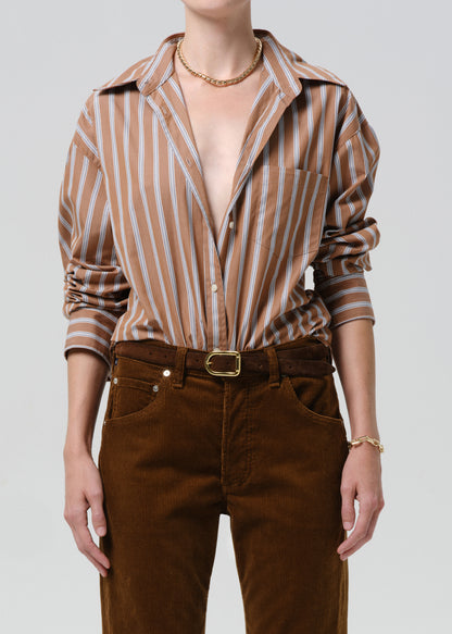 Person wearing a brown and white striped shirt with rolled-up sleeves and brown pants on a grey background