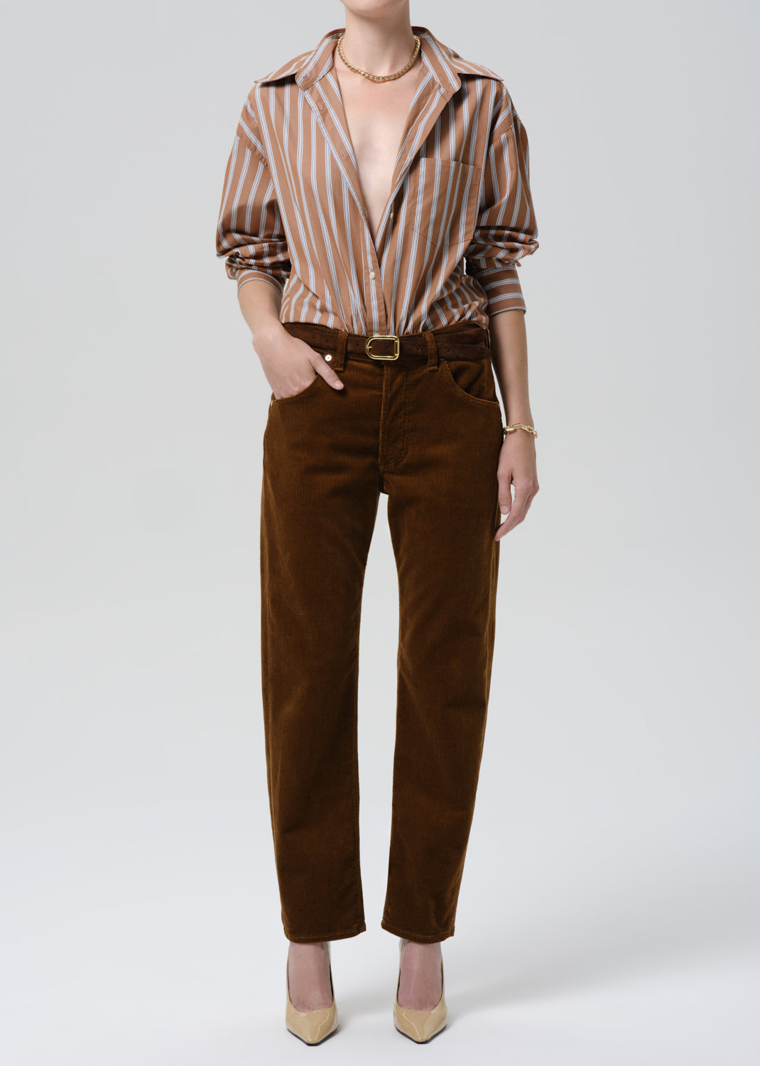 Person wearing a striped shirt and brown pants on a grey background