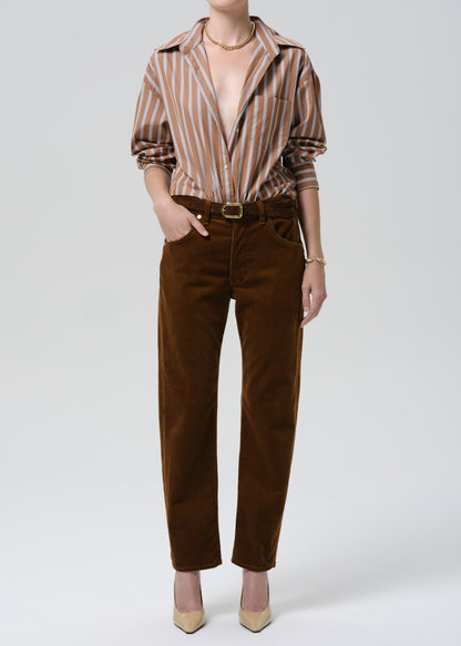 Person wearing a striped shirt and brown pants on a grey background