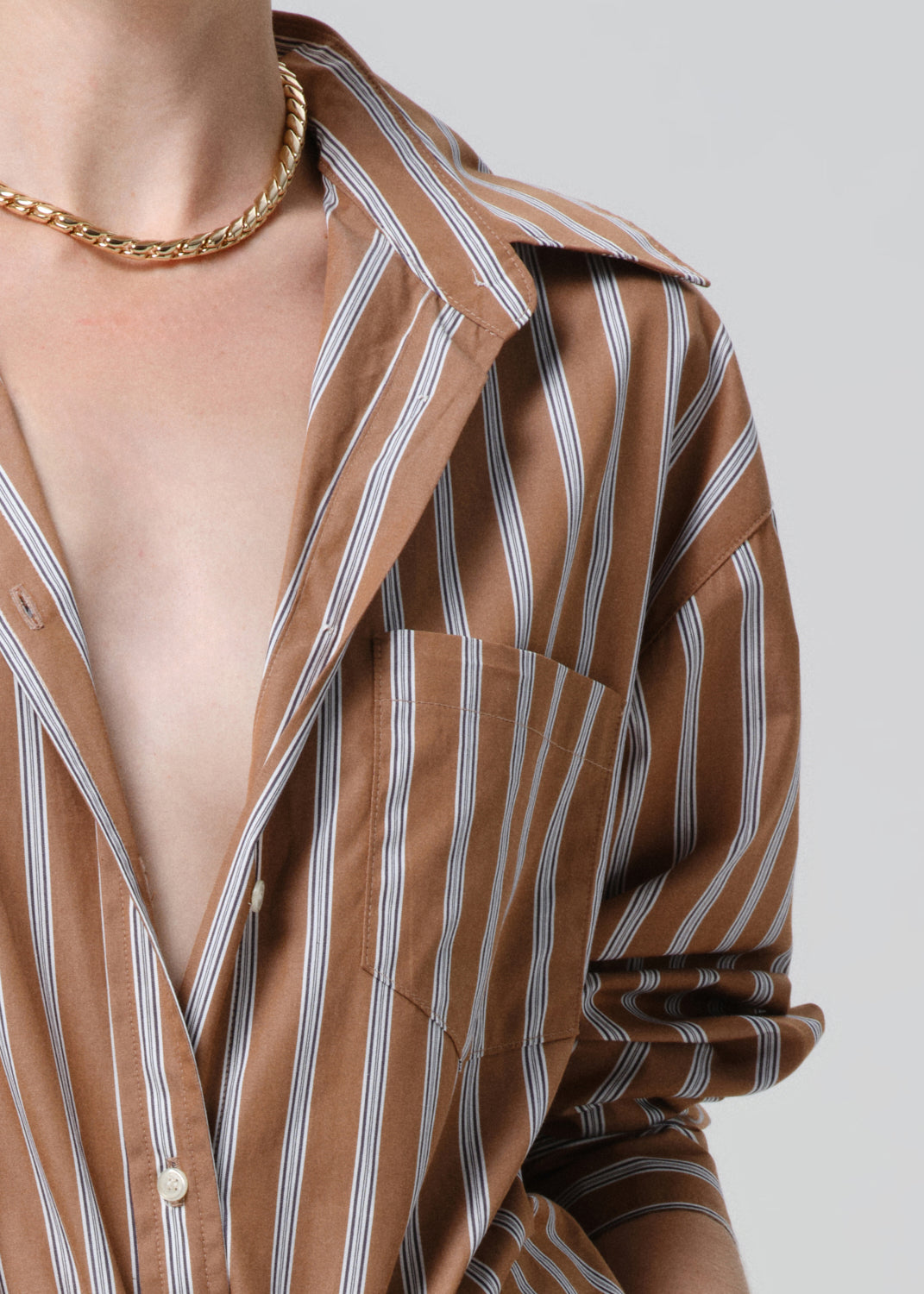 Brown and white striped shirt with a gold chain necklace on a grey background