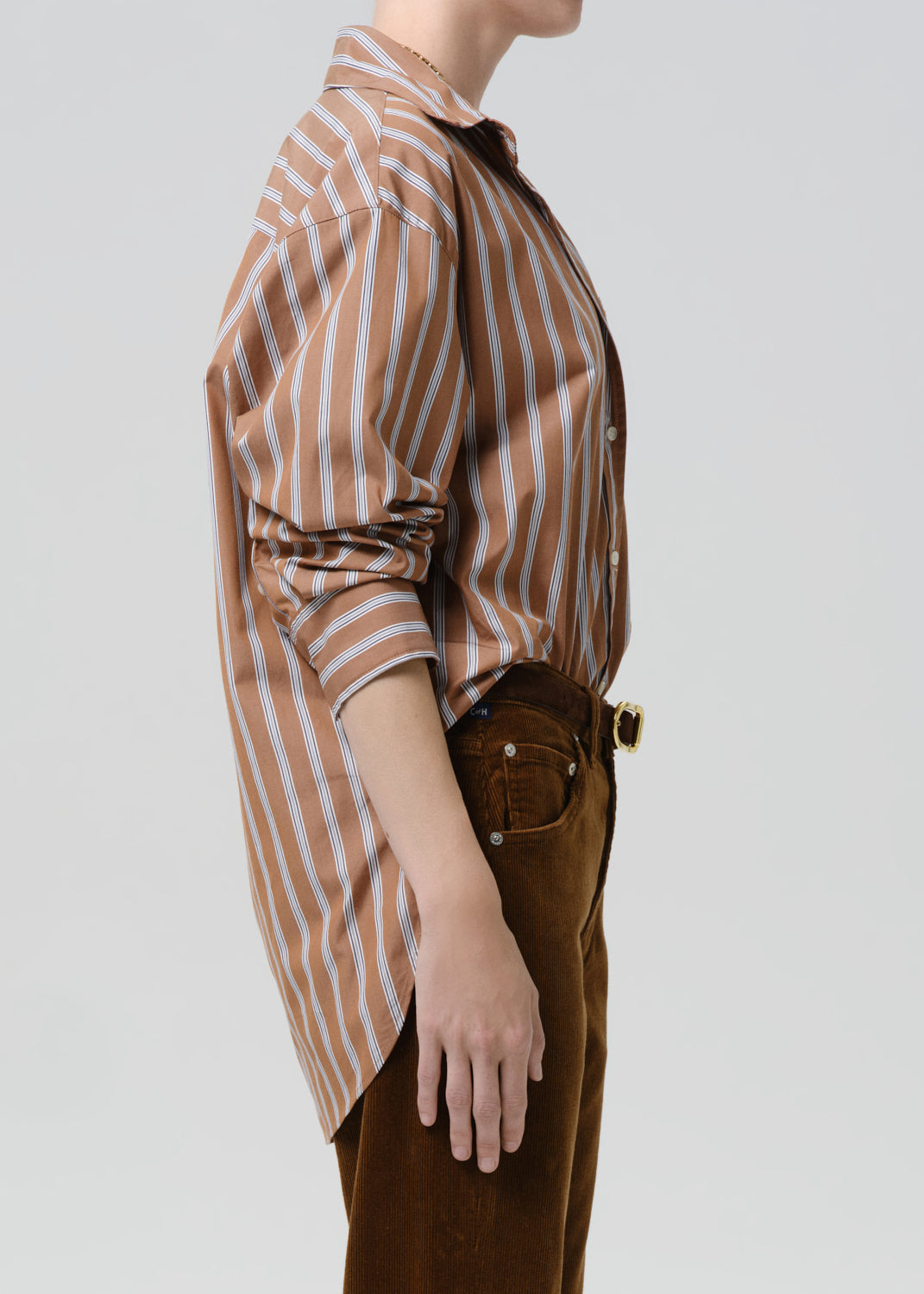 Person wearing a brown and white striped shirt with brown pants on a grey  background