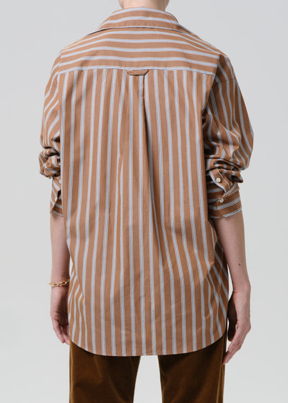 Person wearing a brown and white striped shirt with rolled-up sleeves on a grey background