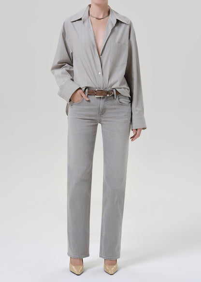 Person wearing a light grey striped button front blouse with light grey straight leg jeans on a grey background