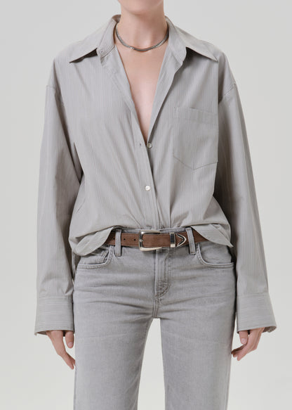 Person wearing a light grey striped button front blouse with light grey straight leg jeans on a grey background