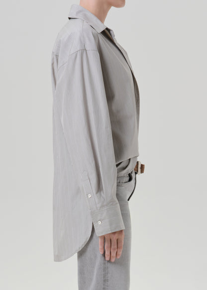 Person wearing a light grey striped button front blouse with light grey straight leg jeans viewed from the side on a grey background