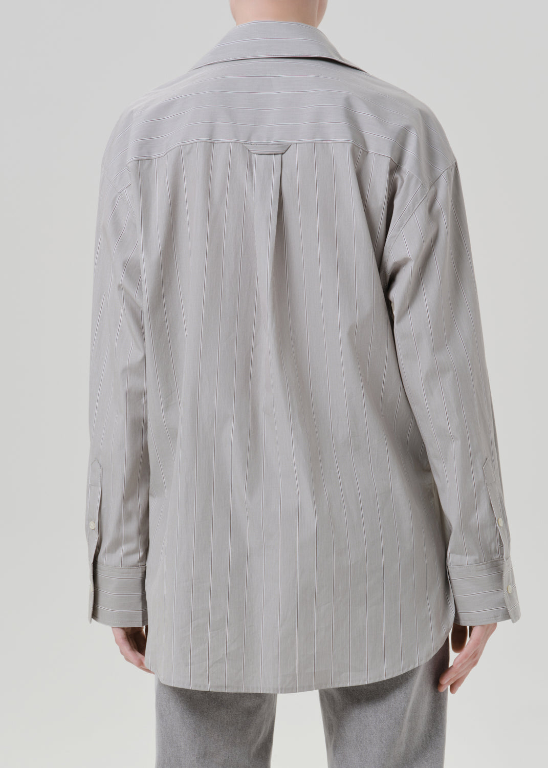 Person wearing a light grey striped button front blouse with light grey straight leg jeans viewed from the back on a grey background