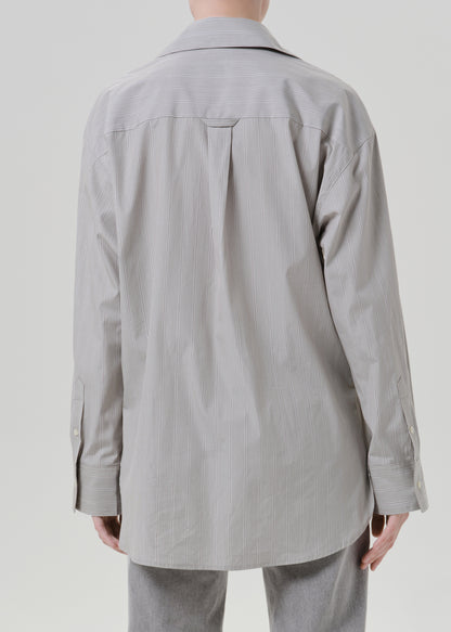 Person wearing a light grey striped button front blouse with light grey straight leg jeans viewed from the back on a grey background