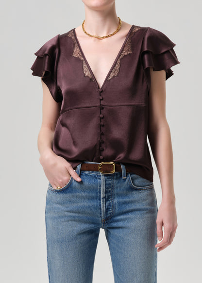 Woman wearing a brown satin top with ruffled sleeves and blue jeans on a grey background