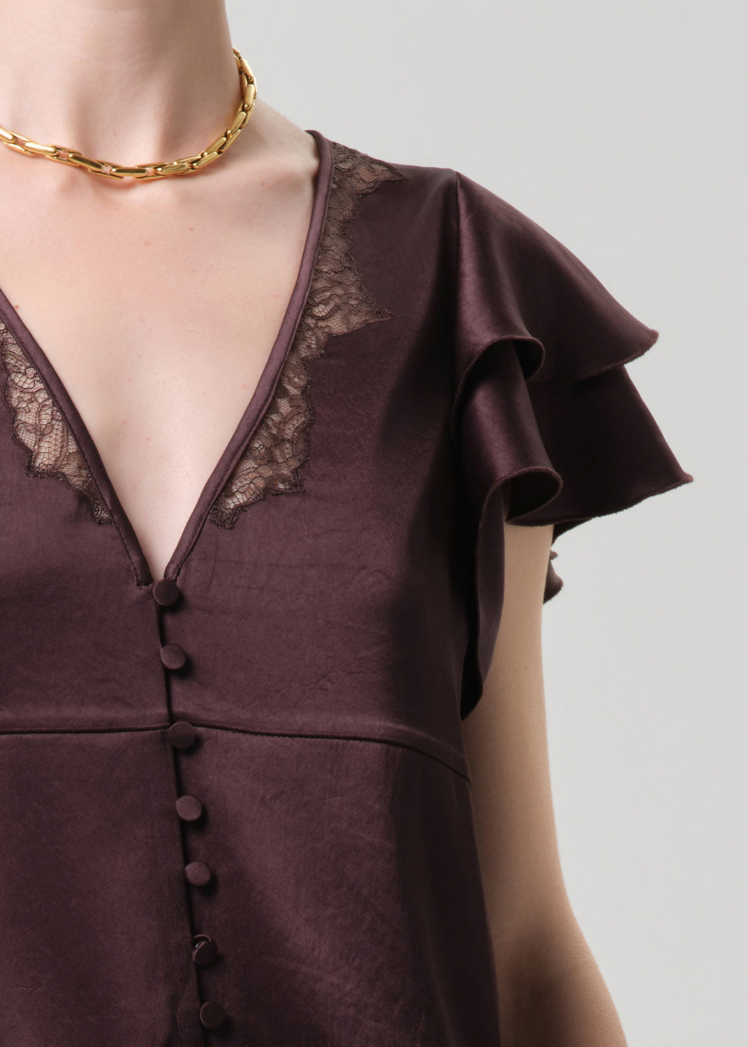 Brown dress with lace details and a gold necklace on a grey background