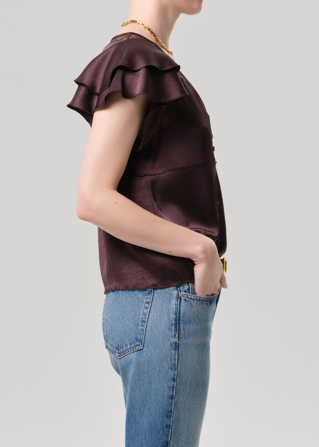 Person wearing a brown top with ruffled sleeves and blue jeans on a grey background