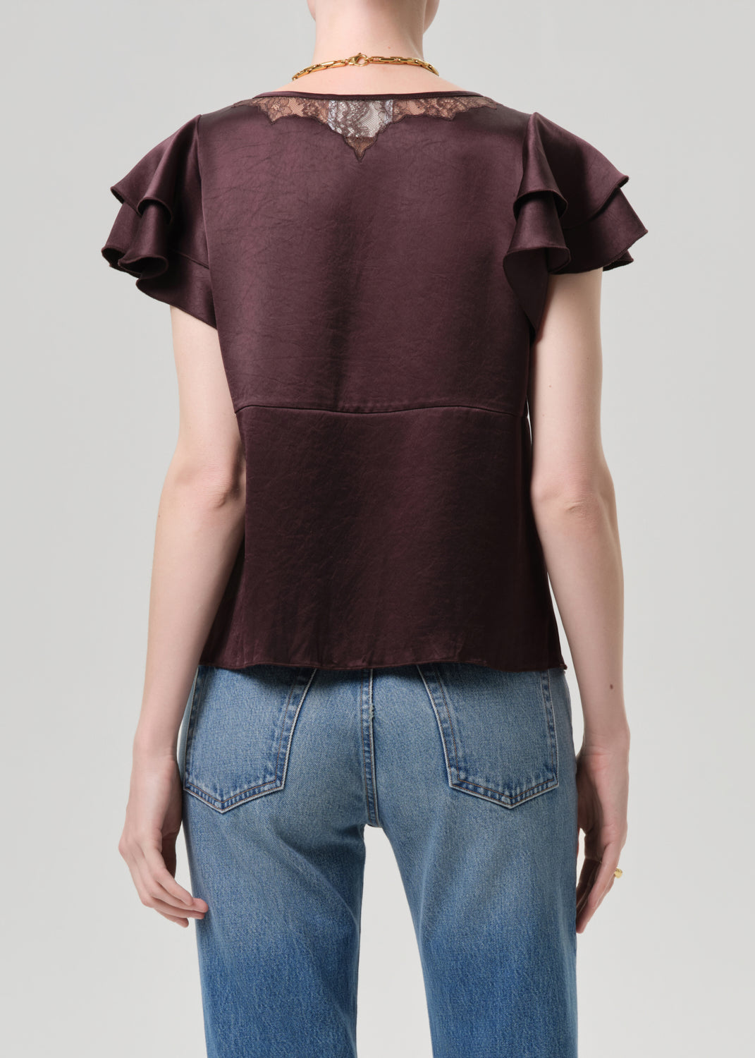 Person wearing a brown top with ruffled sleeves and blue jeans on a grey background