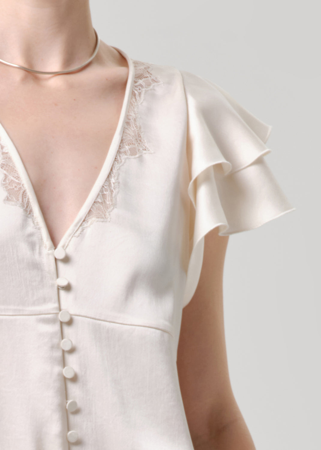 Close-up of a white lace-trimmed top with buttons on a grey background