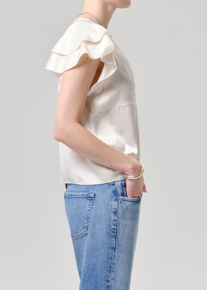 Person wearing a white blouse with ruffled sleeves and blue jeans on a grey background