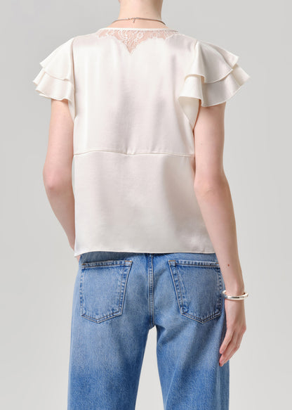 Person wearing a white blouse with ruffled sleeves and blue jeans on a grey background